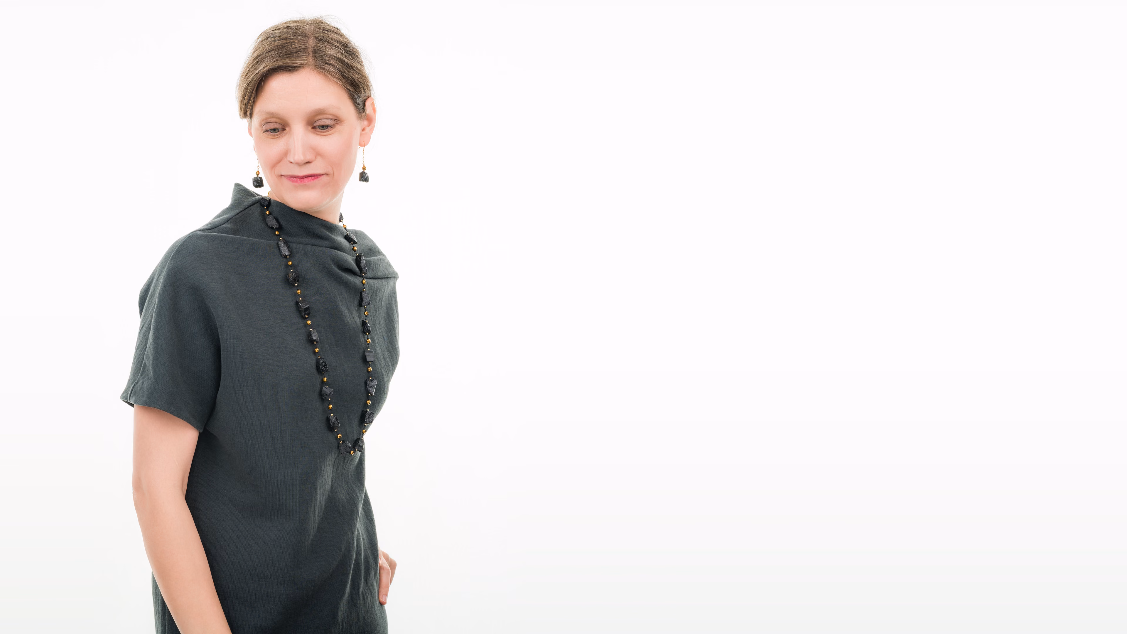 Frau in dunkelgrünem Kleid mit langer Halskette und Ohrringen von Senai Jewels